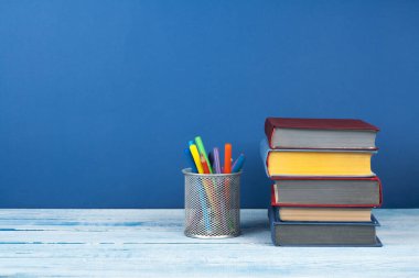 Kitap istifleme. Açık kitap, ahşap masa ve mavi arka plan üzerine ciltli kitaplar. Okula dönelim. Metin için alanı kopyala