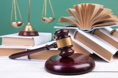 Hukuk konsepti - açık hukuk kitabı, yargıç tokmağı, teraziler, mahkeme salonundaki ya da kolluk kuvvetlerindeki heykel. Tahta masa, yeşil arkaplan.