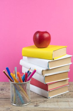 Kitaplar istifleniyor. Tahta masadaki kitaplar ve pembe arka plan. Okula dönelim. Reklam metni için alanı kopyala