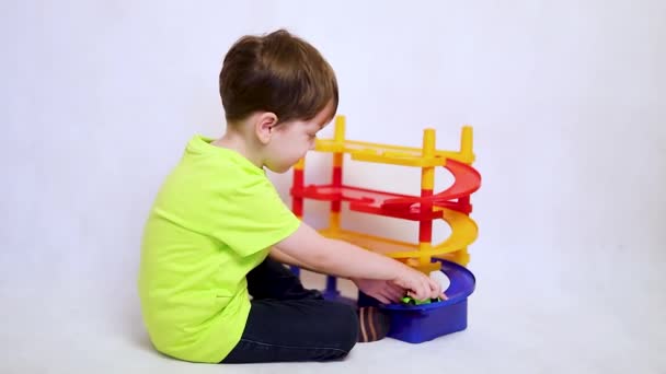 Jongen speelt met auto 's op de parkeerplaats. Kinderspeelgoed. Een jongen speelt met speelgoed op een witte achtergrond. Heldere parkeerplaats voor auto 's. — Stockvideo