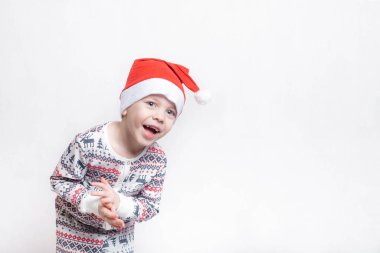 Noel Baba şapkalı çocuk gülüyor. Beyaz arka planda bir çocuk. Kırmızı şapka. Ren geyiği pijaması. Beyaz arka plan. Bir çocuğun duyguları.