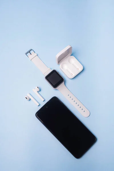 The layout of the watch and the phone on a blue background. Appliances and electronics. Modern gadgets. Phone headphones watch. Business. Student. Wireless headphone. Watch with pedometer. Copy space