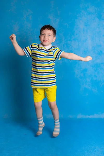 男孩在蓝色的背景上跳跃 孩子的情感 有趣的男孩在一个跳跃 快乐的童年孩子穿上鲜艳的衣服 条纹T恤 — 图库照片