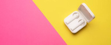 Pembe arka planda kablosuz kulaklık. Parlak bir arka plan. Beyaz kulaklıklar. Bluetooth kulaklık. Pembe ve sarı arka plan. Uzayı kopyala Teknoloji hakkında bir makale. Modern teknolojiler.