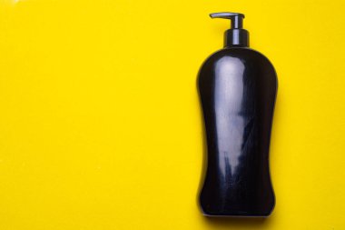Kopyalama alanının arka planında siyah şampuan. Bir şişe şampuan. Sarı arka plan. Güzellik endüstrisi hakkında bir makale. Sarı arka planda şampuan.