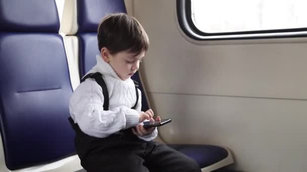 Un garçon joue avec son téléphone en voyage. Des enfants modernes. Bébé et gadgets modernes. Jeux sur votre téléphone. Loisirs sur le voyage. — Video