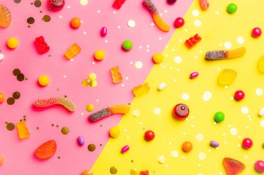 Şekerleme çeşitleri. Sarı-pembe arka planda şekerlemeli düzen. Çiğnenmiş marmelat ve küçük karamel. Parlak bir arka plan. Her tat için tatlı. Tatlılar hakkında bir makale.