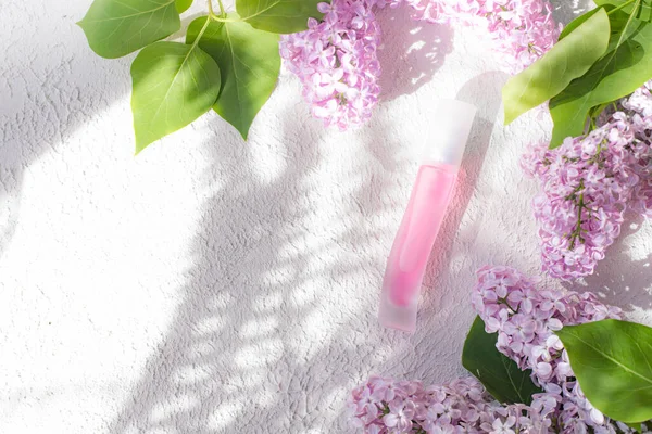 Pink perfume bottle and lilac branch light and shade. The concept of advertising perfumes. A bottle of perfume without text. Floral aromatherapy layout . Copy space