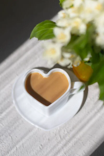 Café cappuccino em uma xícara e um buquê com sombras de sol. Uma bebida quente. Pequeno-almoço. Espaço de cópia — Fotografia de Stock