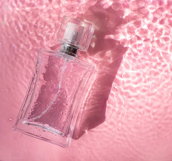Perfume bottle on the background and water drops. A bottle of perfume without inscriptions . Smell. Perfume on a pink background. Water drops. Copy space.