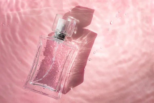 Perfume bottle on the background and water drops. A bottle of perfume without inscriptions . Smell. Perfume on a pink background. Water drops. Copy space. Article about the choice of perfume