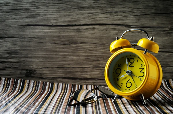 Reloj despertador retro amarillo y anteojos en estera de color aislado w —  Fotos de Stock