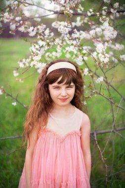 Küçük kız güneşli bir bahar gününde çimenlerin ve çiçeklerin arkasında dinleniyor.