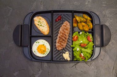 Kahvaltı, biftek ya da pirzola, domatesli ve yeşil sebzeli salata, tost, patates, siyah tabakta yumurta. Sağlıklı beslenme, diyet, menü, iyi beslenme.