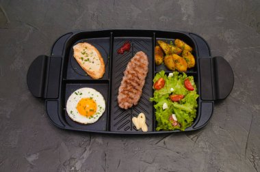 Kahvaltı bifteği ya da pirzola, domatesli ve yeşil sebzeli salata, kızarmış ekmek, patates, yumurta, üstten manzara, koyu arka plan. Sağlıklı beslenme, beslenme, menü, besleyici gıdalar.