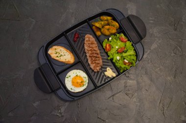 Kahvaltı bifteği ya da pirzola, domatesli ve yeşil sebzeli salata, kızarmış ekmek, patates, yumurta, üstten manzara, koyu arka plan. Sağlıklı beslenme, beslenme, menü, besleyici gıdalar.