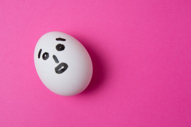 Pembe arkaplanda şaşırmış bir yüz ve kopyalama alanı olan yumurta