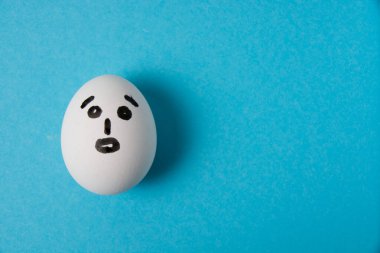 Şaşırmış bir suratı olan yumurta. Mavi arkaplanda izole et.