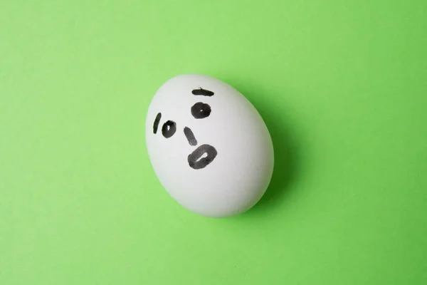 Un huevo con una cara sorprendida, sobre un fondo verde con espacio para copiar. — Foto de Stock