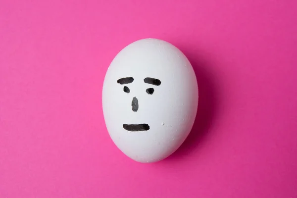 Huevo con una cara indiferente, sobre un fondo rosa con espacio para copiar. — Foto de Stock