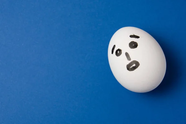Huevo con una cara sorprendida sobre un fondo azul con espacio para copiar. — Foto de Stock