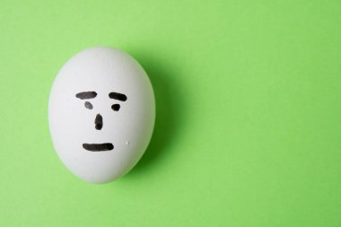 Yüzünde kayıtsız bir duygu olan bir yumurta, yeşil arka plan fotokopi alanı