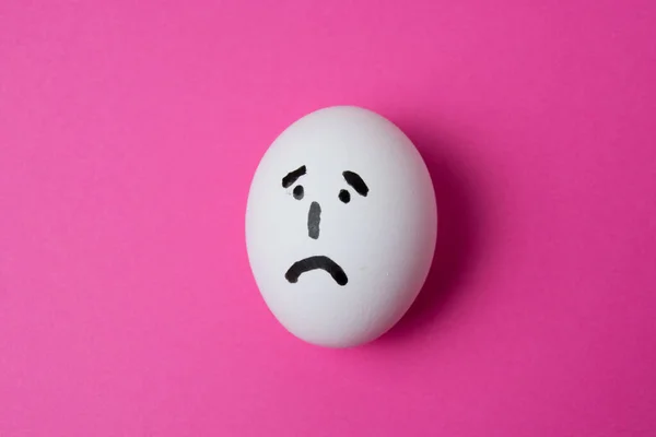 An egg with a sad face, on a pink background with copy space