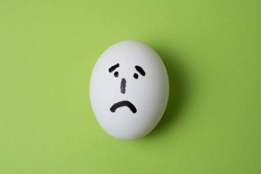 Üzgün yüzlü yumurta, yeşil arka planda kopya alanı ile.