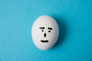 Umursamaz yüzlü bir yumurta. Mavi arka planda izole edin. Yüzündeki umursamazlık duygusu