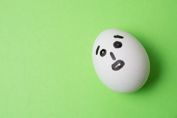 Un huevo con una cara sorprendida, sobre un fondo verde con espacio para copiar. — Foto de Stock