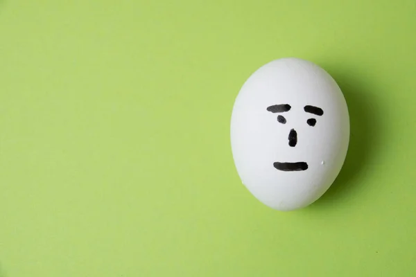 Un huevo con una cara indiferente, sobre un fondo verde con espacio para copiar — Foto de Stock
