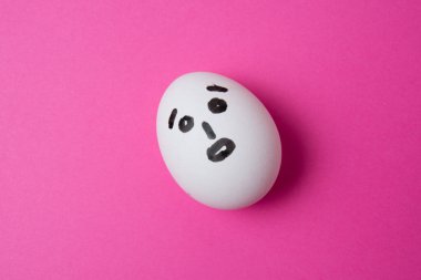 Pembe arkaplanda şaşırmış bir yüz ve kopyalama alanı olan yumurta