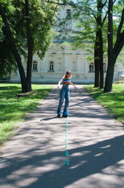 Güzel kız yazın parkta paten kayarken, vyponyaet numaraları yaparken ve çipleri gezerken eğleniyor..