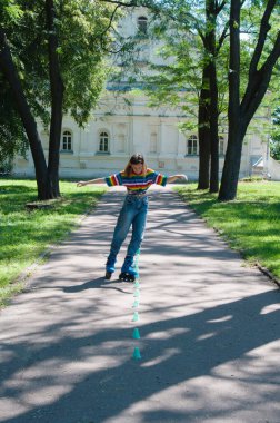 Güzel kız yazın parkta paten kayarken, vyponyaet numaraları yaparken ve çipleri gezerken eğleniyor..
