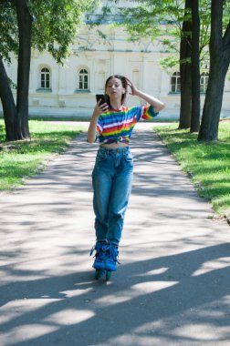 Kulaklıkla paten kayan çok güzel bir kız. Şehir parkında akıllı telefonuyla müzik dinliyor ya da konuşuyor.