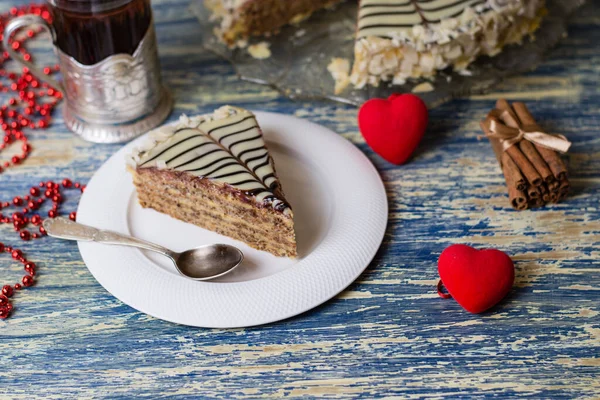 Un délicieux morceau de gâteau avec des noix, des amandes, de la crème et du chocolat, du thé dans un verre et du cœur de krasnyeoe sur un fond en bois bleu clair. Concept de célébration de la Saint-Valentin et relation sérieuse — Photo