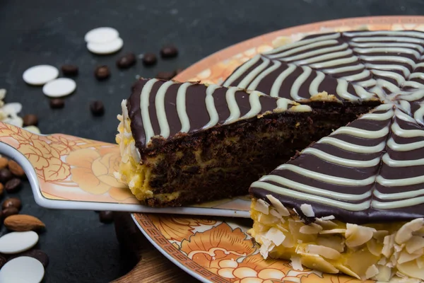 Gâteau esterhazy tranché au chocolat avec crème, glaçage, noix et amandes en gros plan sur une assiette brun orangé sur un fond de béton foncé — Photo