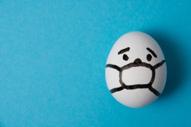 Yüzü maskeli bir yumurta. Mavi arka planda izole edin. Covid 19 ve karantina konsepti.