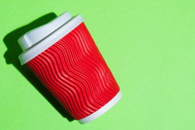 Kahve için kırmızı kağıt bardak ya da yeşil arka planda çay. Fotokopi alanı olan renkli bir arkaplanda tek kullanımlık tablo yazılımı