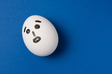 Mavi arkaplanda şaşırmış bir yüz ve kopyalama alanı olan yumurta