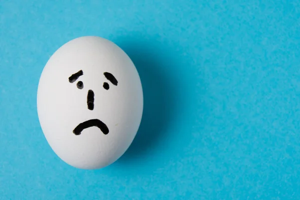 An egg with a sad face. Isolate on a blue background