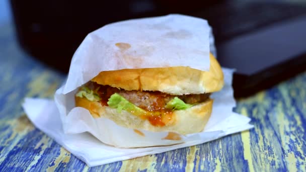 Hamburguesa con carne, verduras y salsa en la mesa cerca del portátil. El concepto de trabajar de forma remota y entregar comida de un restaurante durante la cuarentena — Vídeos de Stock