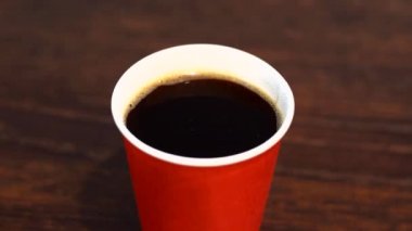 Koyu ahşap masada kırmızı kağıt bardakta kahve.