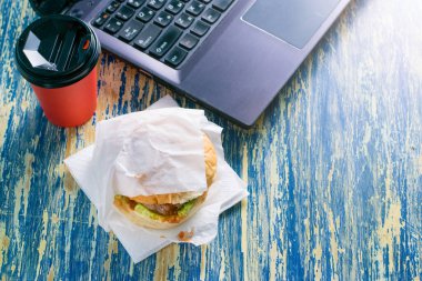 Hamburger, köfte, sos ve salata torbası, kırmızı kağıt bardakta kahve ve dizüstü bilgisayar manzaralı fotokopi alanı. Yemek teslimatı konsepti, karantina bölgesi 19 'daki restoranlar..