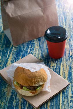 Sığır pirzolası, sos ve salatayla birlikte hamburgerler kağıt bardakta yiyecek ve kahve için el işi bir çantada ve parlak mavi arka plan fotokopi alanında. Yemek teslimatı konsepti, karantina bölgesi 19 'daki restoranlar..