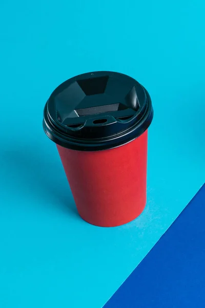 Paper cup with plastic lid on bright blue background copy space.
