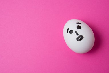 Pembe arkaplanda şaşırmış bir yüz ve kopyalama alanı olan yumurta