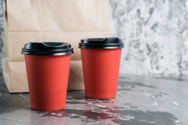 Gri arka plan fotokopi alanındaki el çantalarını götürmek için çay ya da kahve için iki kağıt bardak. Karantina sırasında restoran işletmesinin gelişimi ve gıda teslimatı konsepti..