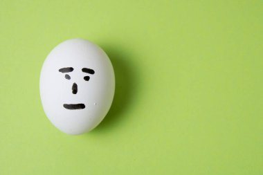 Fotokopi alanı olan yeşil bir arka planda, kayıtsız bir yüze sahip bir yumurta..
