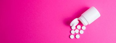 Pembe arka planda fotokopi alanı olan haplar ve beyaz hap kavanozu. Covid 19 tedavi konsepti, afiş biçimi.